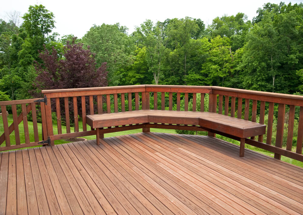 Zenith Builders's deck renovation displaying a chic, slate-grey composite deck flooring that seamlessly blends with classic white railings. The spacious deck is encased in lush greenery, providing a serene outdoor living space with a contemporary feel