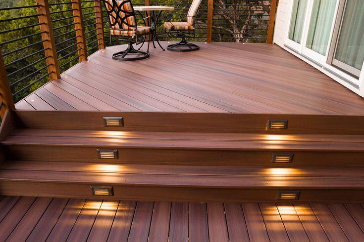 A full deck rebuild by Zenith Builders features a spacious, multi-tier design with luxurious walnut-colored composite planks and contrasting black aluminum balusters, all set against the serene backdrop of a dense, leafy forest