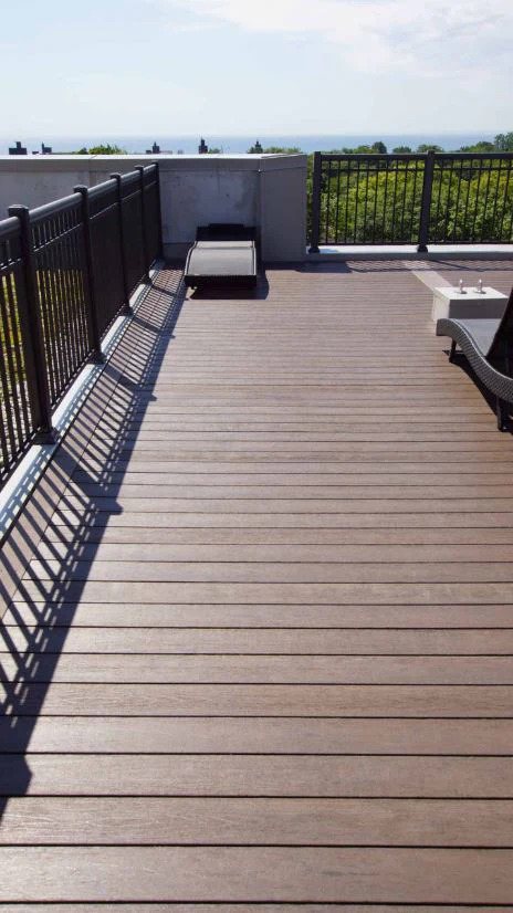 Artfully crafted deck stairs by Zenith Builders with richly stained wooden planks leading down to a charming garden path. The railings are adorned with high-quality, black aluminum balusters.