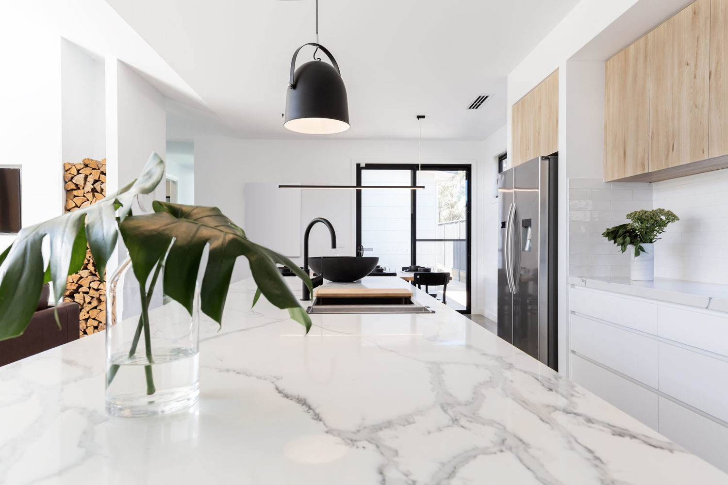 Elegant kitchen sink area remodeled by Zenith Builders, showcasing a deep, undermount sink with a high-arc faucet, set against a luxurious marbled white countertop. The linear mosaic tile backsplash in shades of grey adds sophistication, while the window frames a serene, snowy landscape